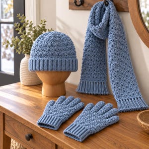 May include: A light blue crochet set consisting of a beanie with a ribbed brim, a long scarf with fringed ends, and a pair of matching gloves with ribbed cuffs. Each piece features a consistent star-like textured stitch pattern throughout the design.
