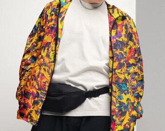 Puede incluir: Una persona con una chaqueta estampada y colorida con una riñonera negra. La chaqueta presenta una vibrante mezcla de amarillo, naranja, morado y azul. La persona también lleva una camiseta blanca y pantalones negros.