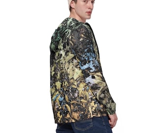 Puede incluir: Chaqueta con capucha con un colorido estampado abstracto en tonos verdes, amarillos, azules y negros. La chaqueta se lleva con vaqueros azules y un gorro beige. El diseño de la chaqueta se asemeja a una mezcla de follaje y pinceladas artísticas.