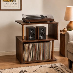 May include: A dark wood record player stand with three tiers. The top tier holds a black turntable with a clear cover. The middle tier features two black speakers. The bottom tier is filled with a collection of vinyl records in colorful sleeves.