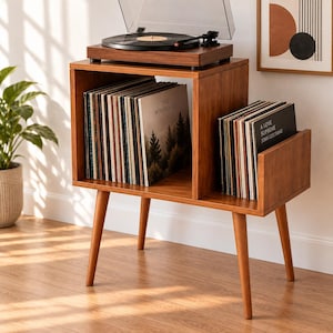 May include: A wooden record player stand with four tapered legs, featuring two open storage compartments filled with vinyl records. A black turntable sits on the top surface. The visible record covers include The Woodlands and A Love Supreme.
