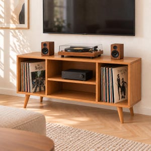 May include: A light brown wooden media console with four tapered legs, featuring two open side compartments filled with vinyl records and a central shelf holding a black audio amplifier, a turntable, and two speakers.