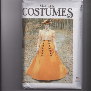May include: A McCall's Costumes sewing pattern envelope M8231 featuring a photograph of a person wearing a long-sleeved yellow and white striped blouse with a bow tie, a matching hat, and a long, solid orange skirt with two vertical rows of black buttons.