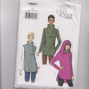 May include: A white Vogue Patterns sewing pattern envelope V8854 featuring illustrations of three tops: a grey sleeveless top with white sleeves, a green long-sleeve top with a high collar, and a magenta long-sleeve hooded top with a high collar.