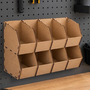 Puede incluir: Un organizador de almacenamiento de madera marrón claro con ocho compartimentos de frente abierto dispuestos en dos filas horizontales de cuatro. La unidad está construida con paneles planos con juntas entrelazadas visibles sobre un panel perforado.