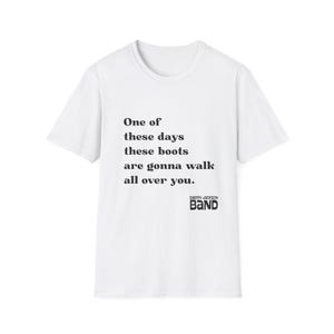 Peut inclure: Un t-shirt blanc à manches courtes avec le texte noir suivant : One of these days these boots are gonna walk all over you. Sous le texte, les mots Cherri Jackson BAND sont imprimés dans une police noire grasse et stylisée sur le devant.