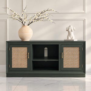 May include: A dark green media console featuring two cabinet doors with light-colored woven cane panels, gold-toned vertical handles, and a central open shelf section. A beige vase with white blossoms and a white torso sculpture sit on top.