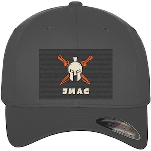Könnte beinhalten: Eine dunkelgraue Baseballkappe mit einem rechteckigen Aufnäher auf der Vorderseite. Der Aufnäher zeigt einen gestickten weißen Spartanerhelm, der über zwei gekreuzten orangefarbenen Schwertern zentriert ist, mit dem Text "JMAC" in weißen Buchstaben.