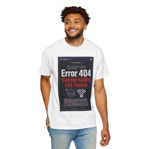 Może przedstawiać: Biały t-shirt z krótkim rękawem z prostokątną grafiką przypominającą okno błędu komputera. Tekst brzmi Error 404 Social skills not found, wraz z ikoną smutnej twarzy, symbolem Wi-Fi oraz polem komunikatu systemowego z przyciskiem OK.