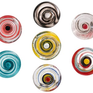 May include: A collection of seven circular glass buttons, each featuring a distinct spiral pattern. The buttons display various colors including red, white, black, yellow, teal, and metallic silver, with some designs being transparent and others opaque.