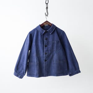 Puede incluir: Una chaqueta de trabajo azul con cuello clásico, mangas largas con puños abotonados y cierre frontal de botones. La prenda incluye un bolsillo en el pecho en el lado izquierdo y dos bolsillos grandes de parche en la parte inferior.
