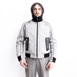 K&ouml;nnte beinhalten: Eine graue Bomberjacke mit schwarzem Besatz und Rei&szlig;verschlusstaschen. Die Jacke hat einen hohen Kragen und einen Rei&szlig;verschluss.
