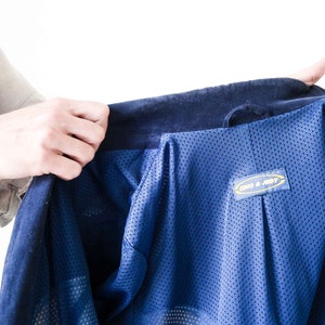 Puede incluir: Una chaqueta azul con forro de malla y una etiqueta amarilla y azul que dice "ONO & JODY".