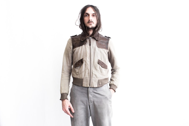 May include: A beige and brown bomber jacket with a zipper closure. The jacket has two pockets on the front and a brown leather collar.
