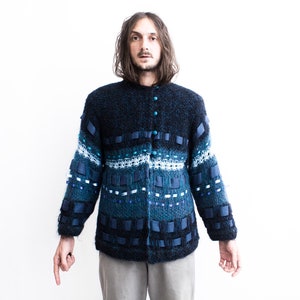 Peut inclure: Un cardigan en tricot bleu avec un motif compos&eacute; d'accents bleus, blancs et noirs. Le cardigan a une fermeture boutonn&eacute;e et des manches longues.