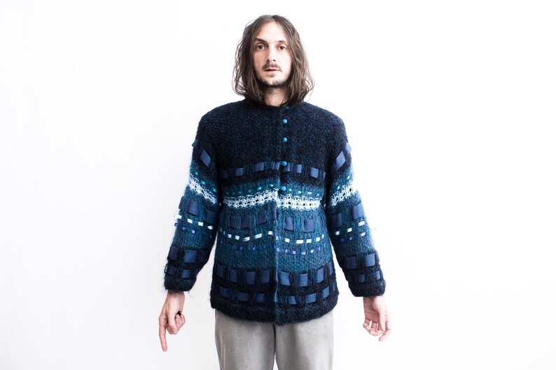 Peut inclure: Un cardigan en tricot bleu avec un motif compos&eacute; d'accents bleus, blancs et noirs. Le cardigan a une fermeture boutonn&eacute;e et des manches longues.