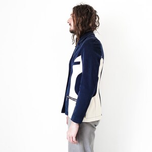 Puede incluir: Una chaqueta azul marino con un dise&ntilde;o geom&eacute;trico blanco y crema en la espalda. La chaqueta tiene una cremallera y un bolsillo en el lado izquierdo.