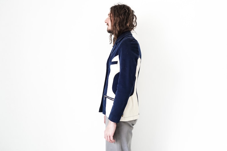 Puede incluir: Una chaqueta azul marino con un dise&ntilde;o geom&eacute;trico blanco y crema en la espalda. La chaqueta tiene una cremallera y un bolsillo en el lado izquierdo.