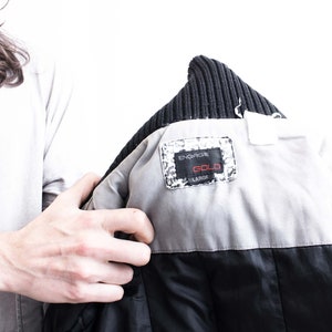 K&ouml;nnte beinhalten: Eine schwarze und graue Jacke mit einem schwarzen Strickkragen. Die Jacke hat ein wei&szlig;es Futter mit einem schwarzen und wei&szlig;en Etikett mit der Aufschrift "ENGORGON GOLD LARGE".