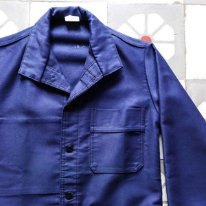 May include: A dark blue work jacket with a button-up front and a single chest pocket. The jacket has a collar and long sleeves.