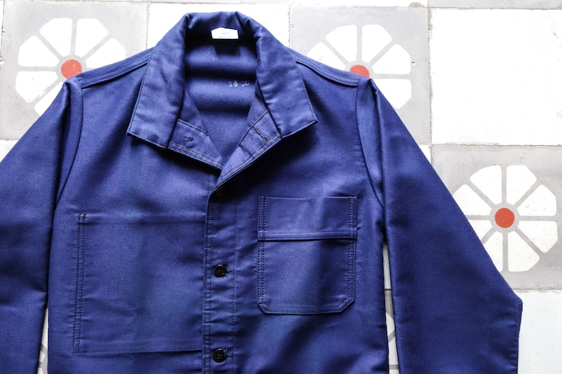 May include: A dark blue work jacket with a button-up front and a single chest pocket. The jacket has a collar and long sleeves.