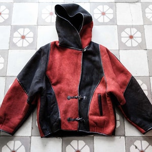 Op de afbeelding: Een rood en zwart hooded jack met een toggle sluiting. De jas is gemaakt van een zacht, suède-achtig materiaal.