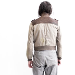 May include: A beige and brown bomber jacket with a ribbed knit collar and cuffs. The jacket has a zipper closure and two pockets.