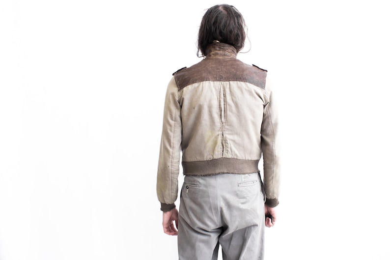May include: A beige and brown bomber jacket with a ribbed knit collar and cuffs. The jacket has a zipper closure and two pockets.