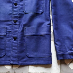 May include: A dark blue work jacket with a button-up front, two chest pockets, and two lower pockets. The jacket has a long sleeve and a collar.