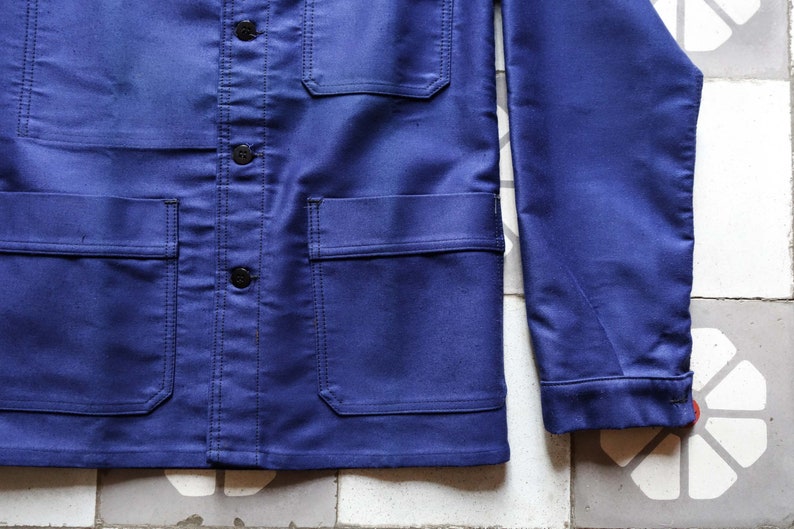 May include: A dark blue work jacket with a button-up front, two chest pockets, and two lower pockets. The jacket has a long sleeve and a collar.
