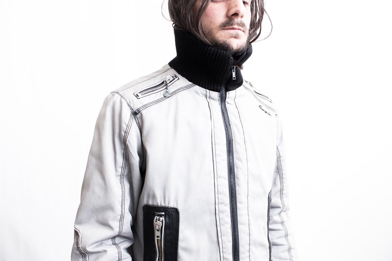 K&ouml;nnte beinhalten: Eine wei&szlig;e Rei&szlig;verschlussjacke mit schwarzen N&auml;hten und einem schwarzen Stehkragen. Die Jacke hat einen Rei&szlig;verschluss und mehrere Taschen.