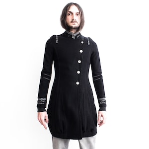 Peut inclure: Un long manteau noir à manches longues avec un col montant et des boutons argentés. Le manteau est orné de surpiqûres décoratives sur les épaules et les poignets.