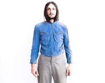 May include: A man wearing a blue suede jacket with a zip fastening and grey trousers.