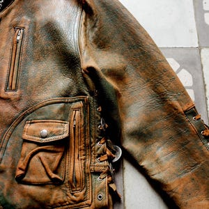 May include: A brown leather jacket with a zip fastening and a lace-up detail on the side. The jacket has a distressed look and a worn-in feel.