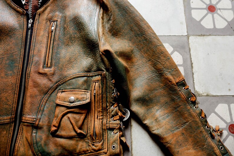 May include: A brown leather jacket with a zip fastening and a lace-up detail on the side. The jacket has a distressed look and a worn-in feel.