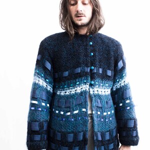 Peut inclure: Un cardigan en tricot bleu et noir avec un design unique comprenant des accents de ruban bleu et des boutons. Le cardigan a un tricot textur&eacute; et une coupe d&eacute;contract&eacute;e.