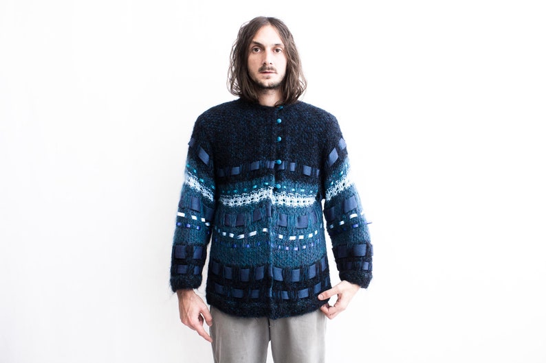 Peut inclure: Un cardigan bleu et noir &agrave; motifs avec une fermeture boutonn&eacute;e. Le cardigan est en tricot textur&eacute; et est d&eacute;cor&eacute; de rubans bleus et blancs.