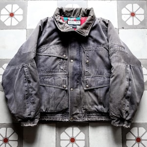 May include: A gray Pacific Trail jacket with multiple pockets and a ribbed hem. The jacket has a collared neckline with a patterned lining and button closures. The jacket is displayed on a tiled surface.