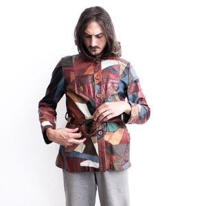 May include: A man wearing a multi-coloured patchwork leather jacket with a brown leather belt. The jacket features a variety of colours and textures, including brown, red, blue, and white.