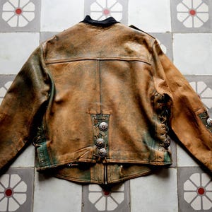 May include: A brown leather jacket with green accents and silver buttons. The jacket has a distressed look and is made of a soft, supple leather.