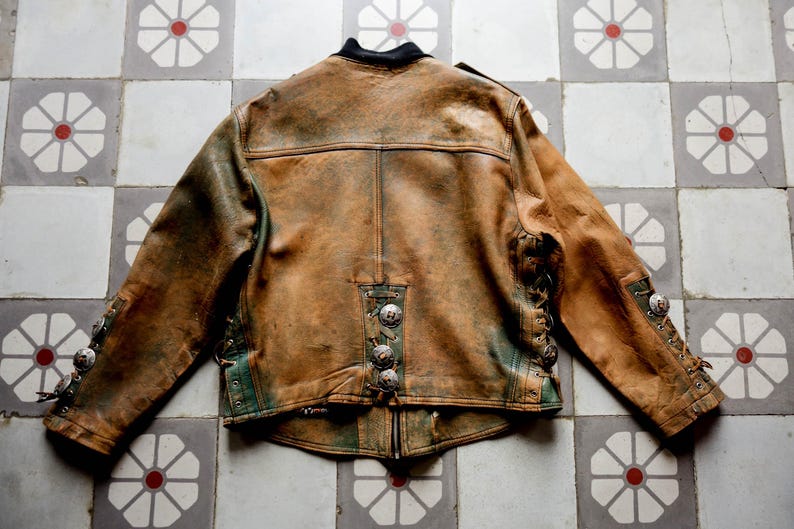 May include: A brown leather jacket with green accents and silver buttons. The jacket has a distressed look and is made of a soft, supple leather.