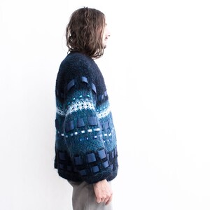 Peut inclure: Un pull bleu et vert &agrave; motifs avec des accents de ruban bleu. Le pull est ample et &agrave; manches longues.