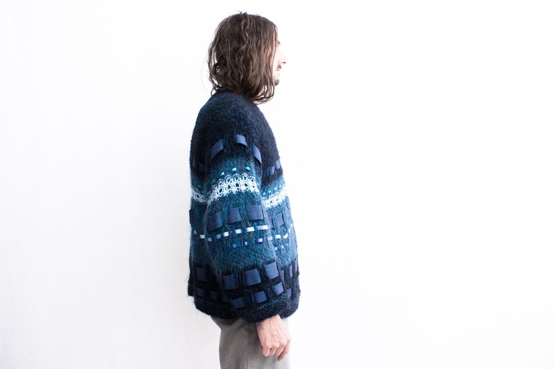 Peut inclure: Un pull bleu et vert &agrave; motifs avec des accents de ruban bleu. Le pull est ample et &agrave; manches longues.