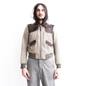 May include: A man wearing a light brown bomber jacket with brown leather accents and gray pants.