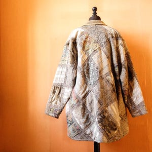 May include: A brown patchwork jacket with a quilted design. The jacket has a collar and long sleeves.