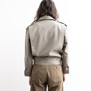 Pu&ograve; includere: Giacca beige chiaro dal design strutturato, con colletto, spalline e vita stretta. La giacca ha maniche lunghe ed &egrave; abbinata a pantaloni marroni. Il modello &egrave; visto da dietro.