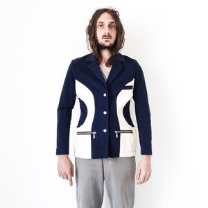 Puede incluir: Una chaqueta azul marino con paneles geom&eacute;tricos blancos y bolsillos con cremallera. La chaqueta tiene cierre de bot&oacute;n.