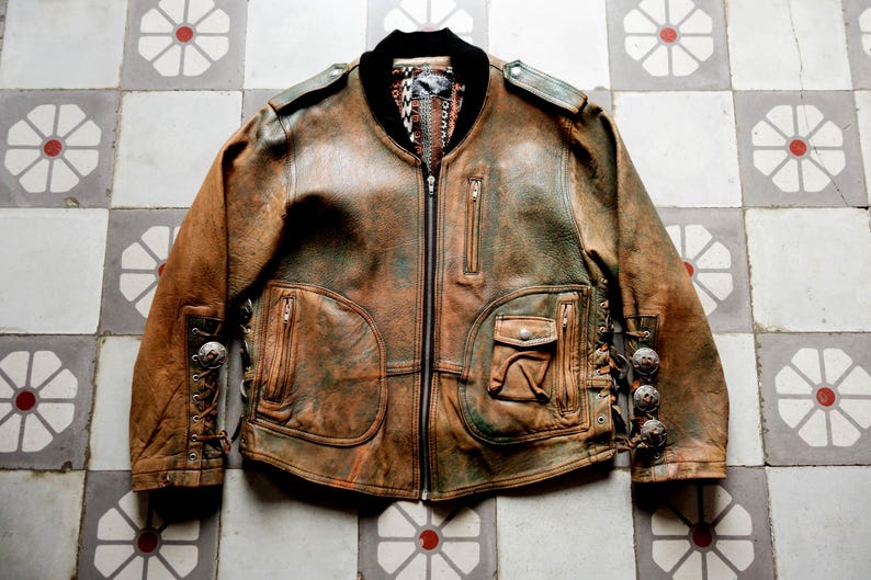 May include: A brown leather jacket with a zip fastening and decorative lacing on the sleeves. The jacket has a distressed look and features multiple pockets.