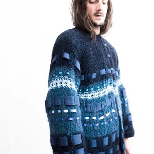 Peut inclure: Un pull en tricot bleu et noir avec un design unique comprenant des rubans bleus et blancs et des carr&eacute;s de tissu.
