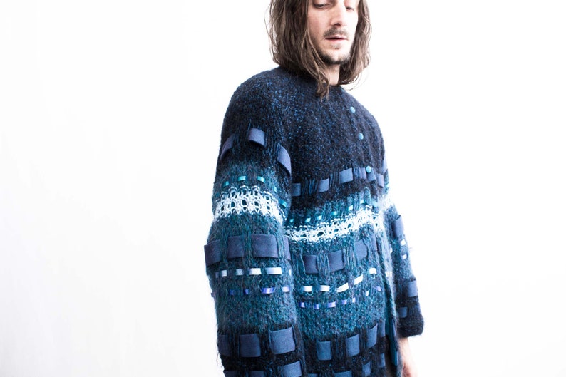 Peut inclure: Un pull en tricot bleu et noir avec un design unique comprenant des rubans bleus et blancs et des carr&eacute;s de tissu.